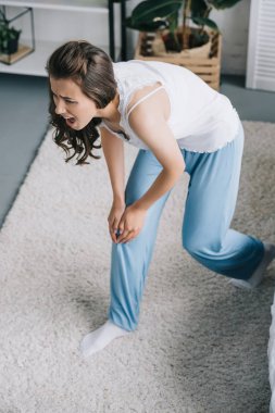 Genç kadının evde diz ağrısı muzdarip pijama yüksek açılı görünüş