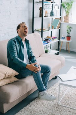 kanepede oturan ve diz ağrısı muzdarip adam