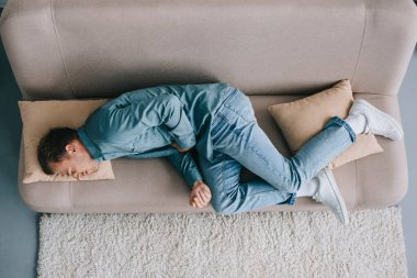 top view of man lying on sofa and suffering from abdominal pain clipart