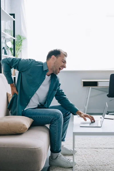 Sidovy Ung Man Lider Smärta Ryggen Medan Använder Laptop Hemma — Stockfoto