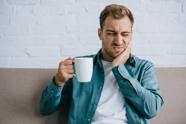 young man holding cup and suffering from toothache