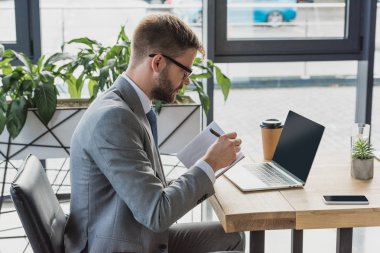 Not defterinde yazılı ve dizüstü bilgisayar kullanma office işadamı yan görünüm