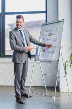smiling young businessman pointing at whiteboard with business charts and graphs clipart