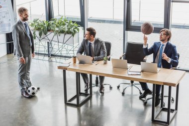 dizüstü bilgisayarlar kullanarak ve office futbol ve basketbol topları ile oynayan genç işadamlarının yüksek açılı görünüş