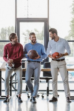 Üç Genç İşadamları basketbol, futbol ve ragbi topları ofiste tutmak gülümseyen