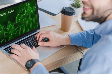 Kırpılan atış ile online ticaret grafikler ekran üzerinde dizüstü kullanarak kulaklık gülümseyen iş adamı 
