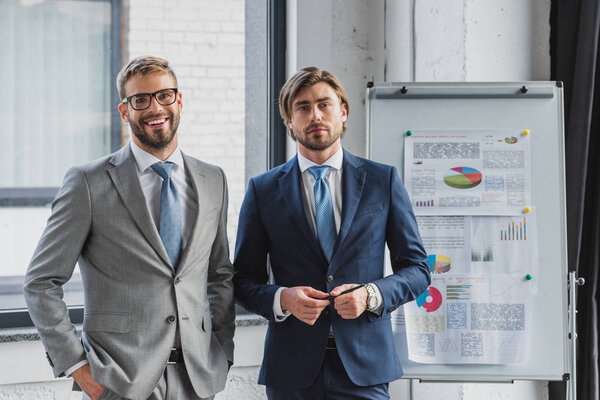 three handsome young businessmen in suits standing together and looking at camera in office