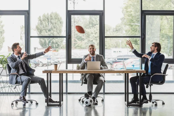 Улыбающиеся Молодые Бизнесмены Пользующиеся Ноутбуками Играющие Футбол Регби Офисе — стоковое фото