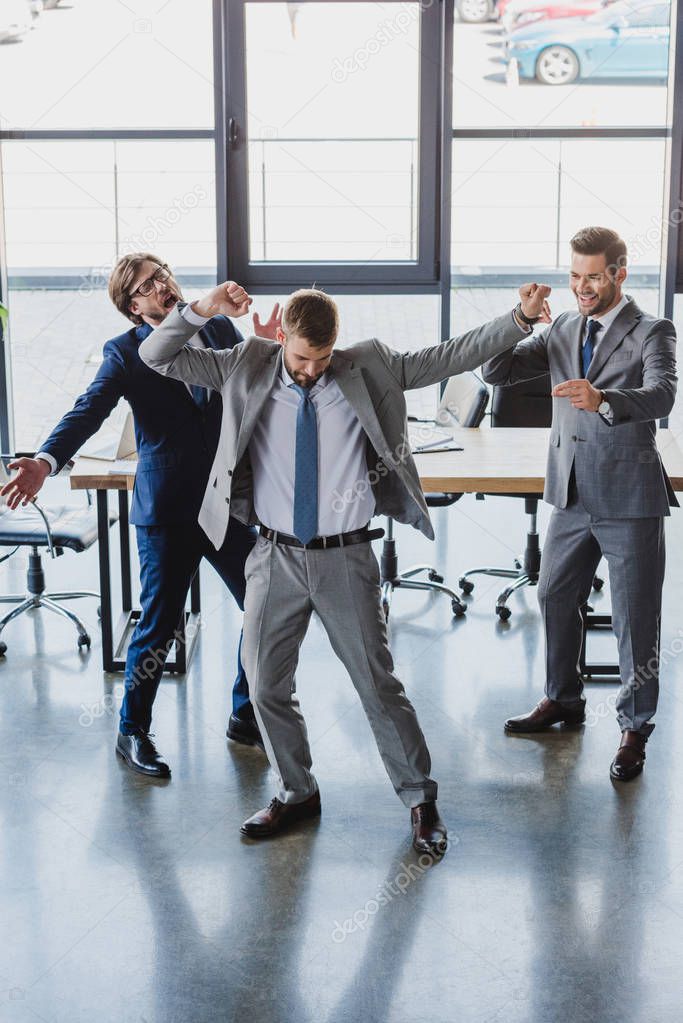 excited young businessmen dancing and celebrating in office 