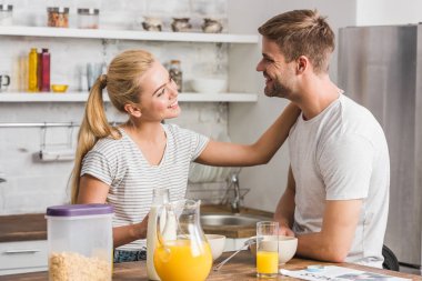 smiling girlfriend touching boyfriend during breakfast in kitchen