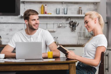 dizüstü bilgisayar kullanarak ve evde kitap okuma kız arıyor kulaklık genç adam gülümseyen