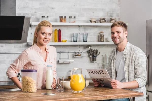 boyfriend holding travel newspaper and looking at camera in kitchen