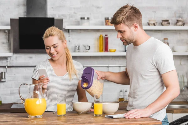 Boyfriend Pouring Cornflakes Plate Breakfast Kitchen Girlfriend Using Smartphone — Free Stock Photo