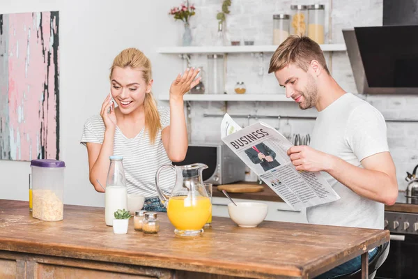 スマート フォンで話していると 新聞を読んで彼氏の台所で朝食時に身振りで示すことのガール フレンド — ストック写真
