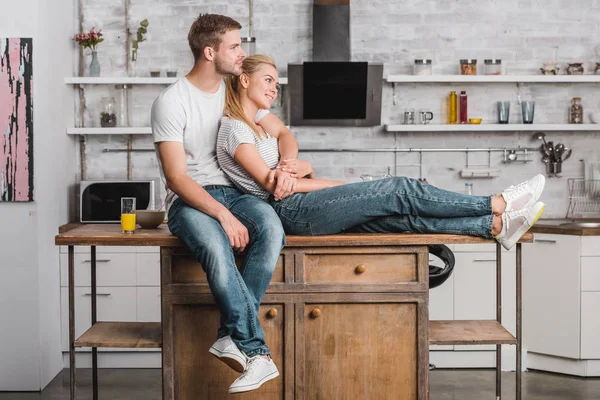 Feliz Pareja Abrazando Mirando Hacia Otro Lado Sentado Mostrador Cocina —  Fotos de Stock