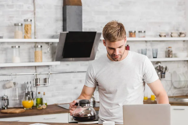 Handsome Man Holding Coffee Pot Looking Laptop Kitchen — Free Stock Photo