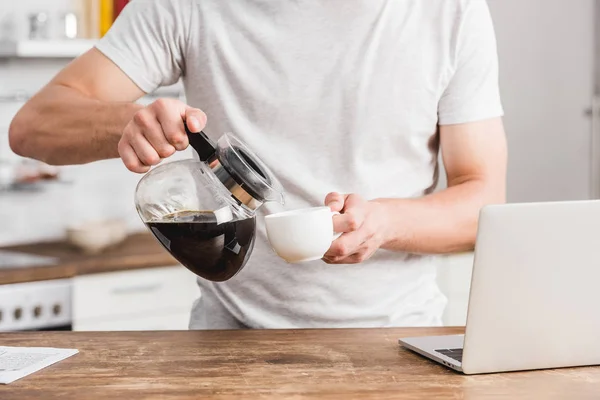 Imagem Cortada Homem Derramando Café Copo Branco Perto Laptop Cozinha — Fotografia de Stock