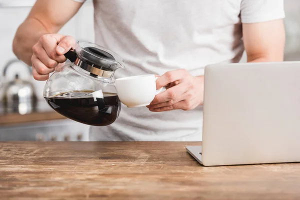 Cropped Image Man Pouring Coffee Coffee Pot Cup Laptop Kitchen — Stock Photo, Image