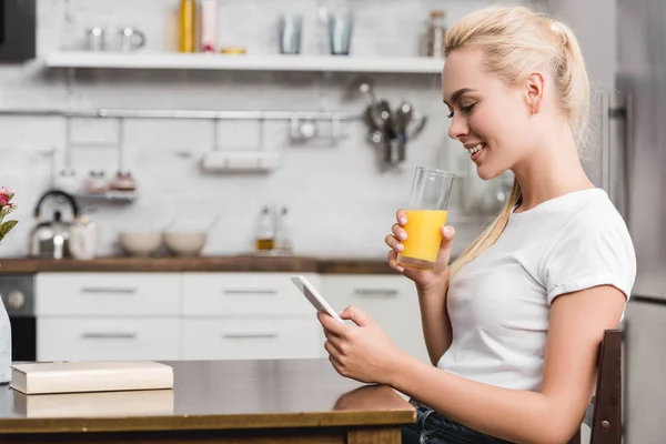 Vista Lateral Sorrir Jovem Bebendo Suco Fresco Usando Smartphone Casa — Fotografia de Stock