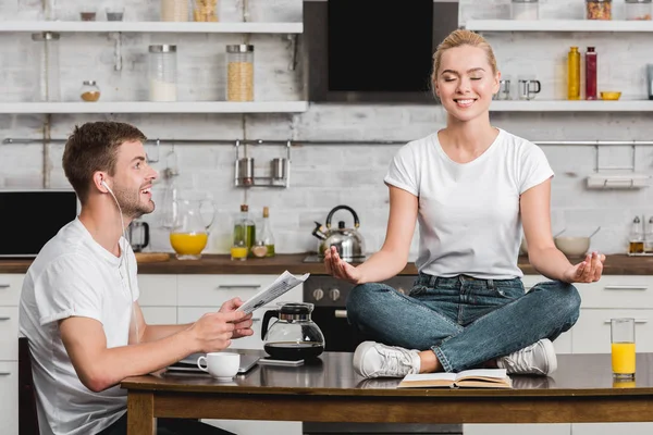 Smiling Young Man Reading Newspaper Looking Happy Girlfriend Meditating Kitchen — Stock Photo, Image