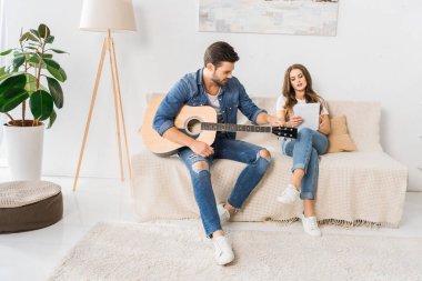 Genç çift kanepe evde dijital tablet ile akustik gitar tuning