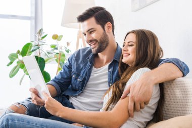 Genç çift dijital tablet vasıl ev ile kanepede oturan gülüyor 