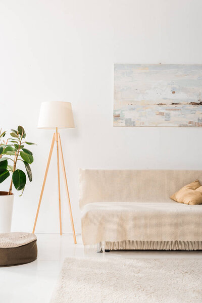 интерьер современной гостиной с лампой, растением, картиной и диваном
