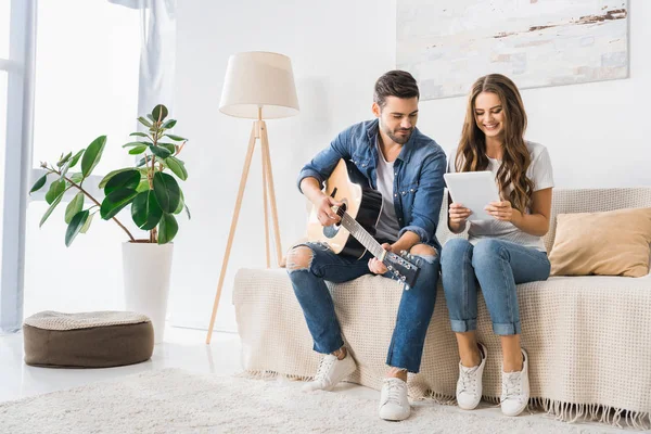 Smiling Couple Tuning Acoustic Guitar Digital Tablet Sofa Home — Stock Photo, Image