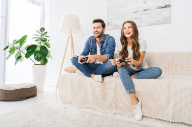 gülen çift evde kanepenin üzerinde joystick tarafından video oyun oynarken 