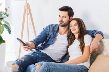 young couple with remote controller watching tv on couch at home 