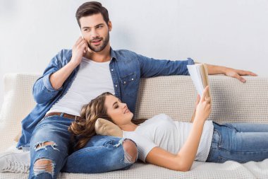 Akıllı kız arkadaşını evde kanepede kitap okuma sırasında konuşan yakışıklı genç adam