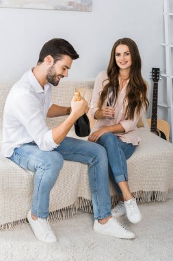 happy young couple celebrating with bottle of champagne and glasses on couch at home
