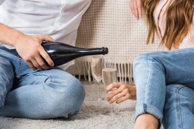 evde kız arkadaşı ile birlikte katta otururken cam içine adam dökme şampanya kadeh kırpılmış