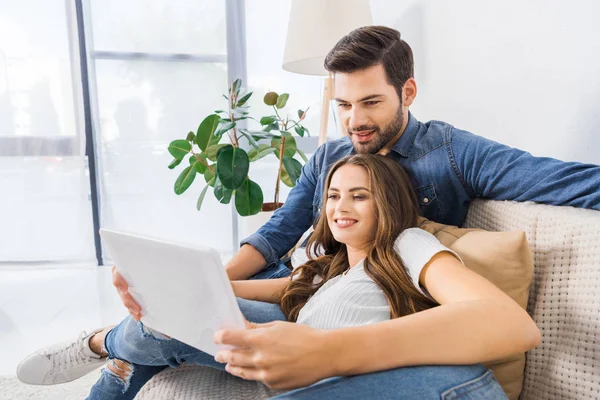 ソファに座って デジタル タブレットの自宅を見て笑顔の若いカップル — ストック写真