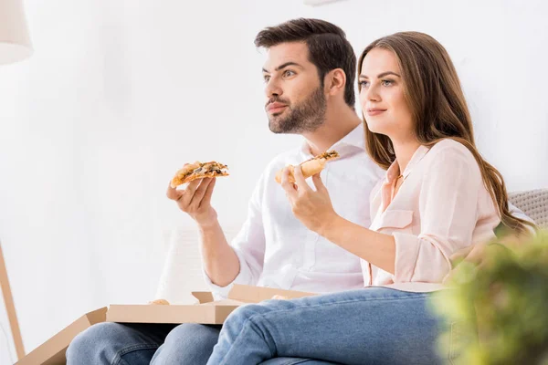 年轻夫妇在家里看电视时吃比萨饼的肖像 — 图库照片