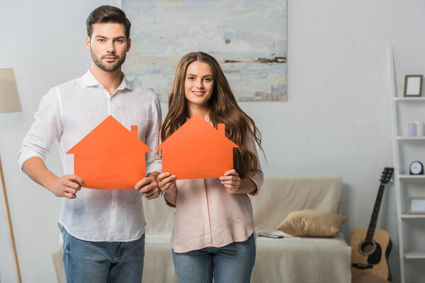 portrait of smiling couple showing paper houses in hands at new home