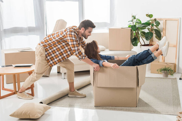 вид сбоку пары, веселящейся с картонной коробкой в новом доме, концепция переезда домой
