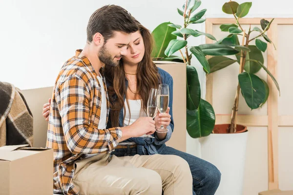 couple in love with glasses of champagne at new house with cardboard boxes, moving home concept