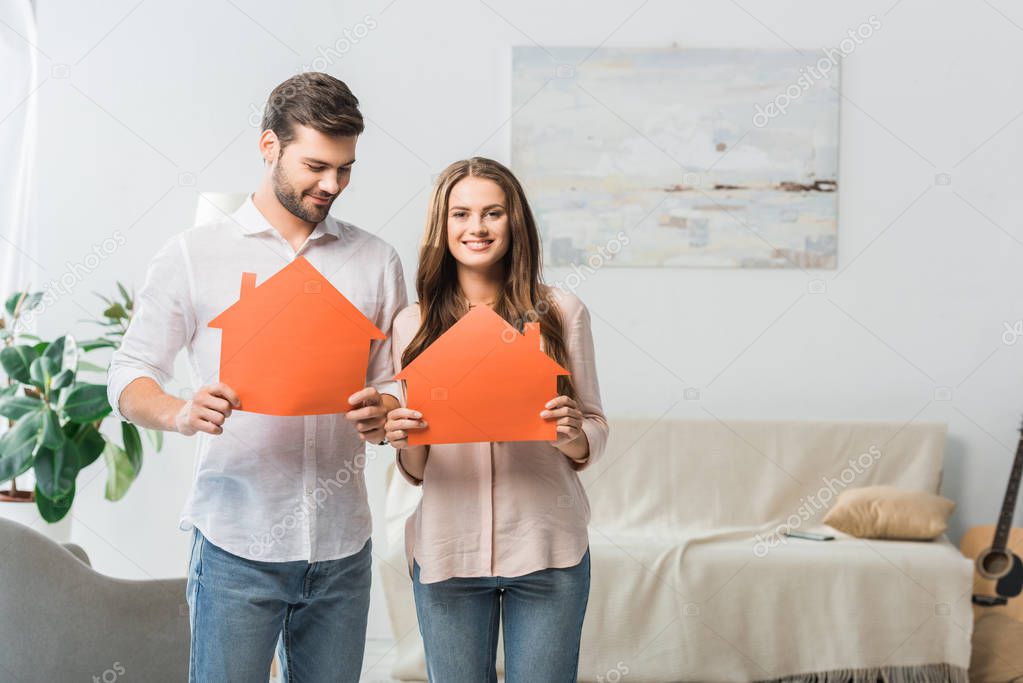 portrait of smiling couple showing paper houses in hands at new home