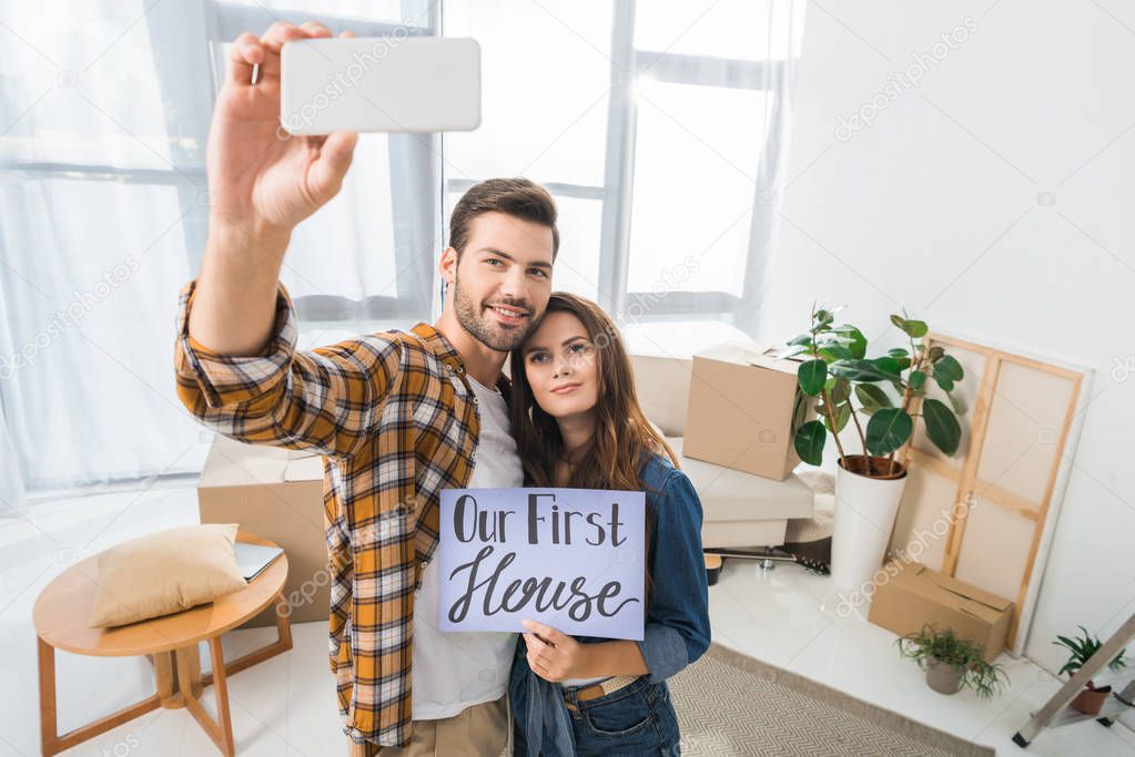 portrait of young couple with our first house card taking selfie on smartphone, moving home concept