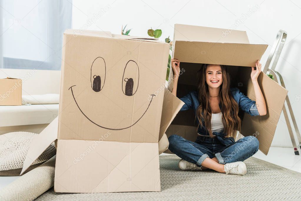 happy woman with cardboard boxes sitting on floor at new home