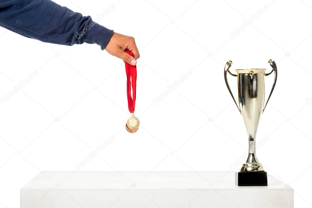 partial view of man holding golden medal near trophy cup isolated on white background 