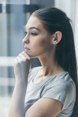 side view of sad young woman with hand on chin looking away clipart