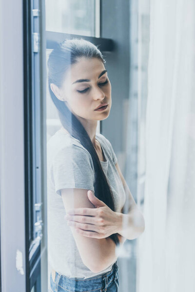 upset young woman with crossed arms leaning at window