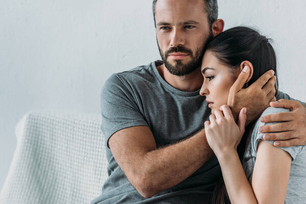 bearded man supporting and hugging depressed woman sitting on couch 