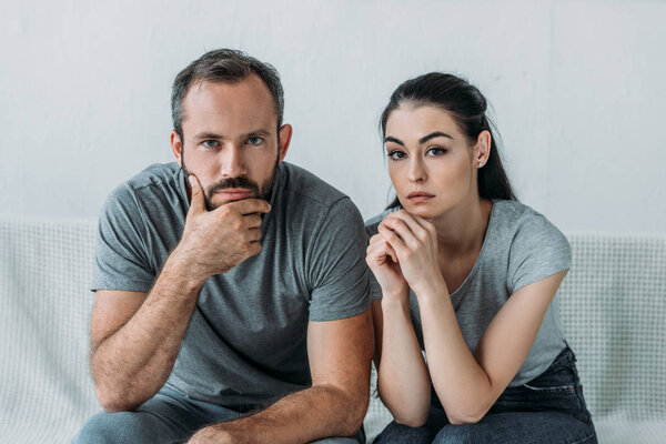 sad couple sitting on couch and looking at camera, relationship difficulties concept