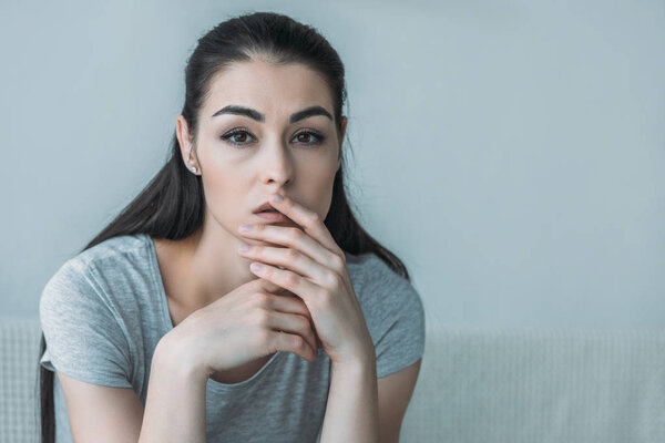 portrait of depressed young woman sitting on couch and looking at camera 