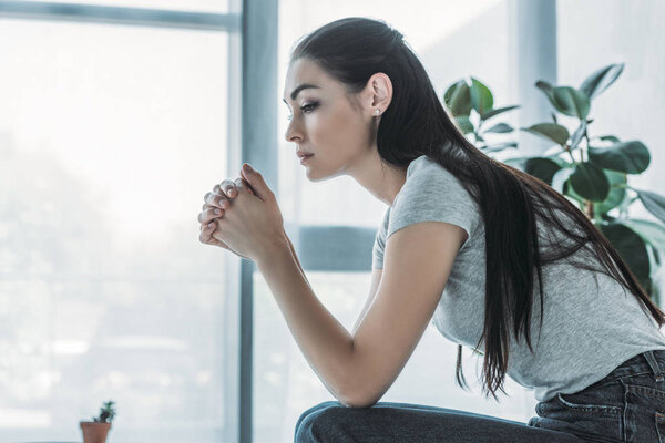 side view of upset brunette woman sitting at home