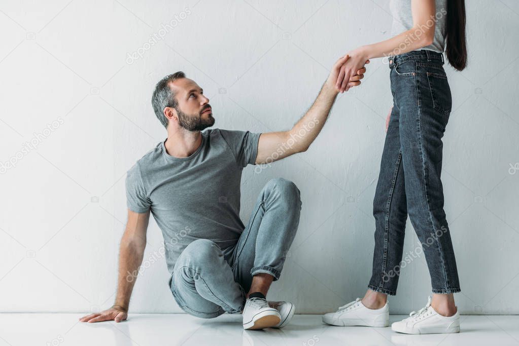 cropped shot of young woman giving hand to depressive bearded man sitting on floor