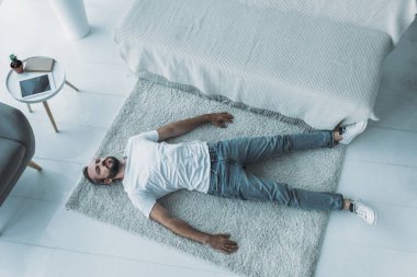 top view of sad bearded middle aged man with depression lying on carpet at home